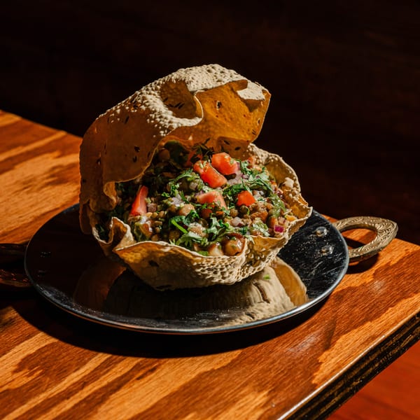 Indian chaat, a lentil and vegetable salad, served in a crispy papadum bowl on a metal plate.