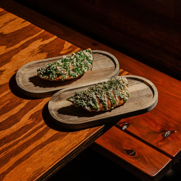 Two Indian flatbreads with green and white toppings on wooden serving trays on a wooden table.