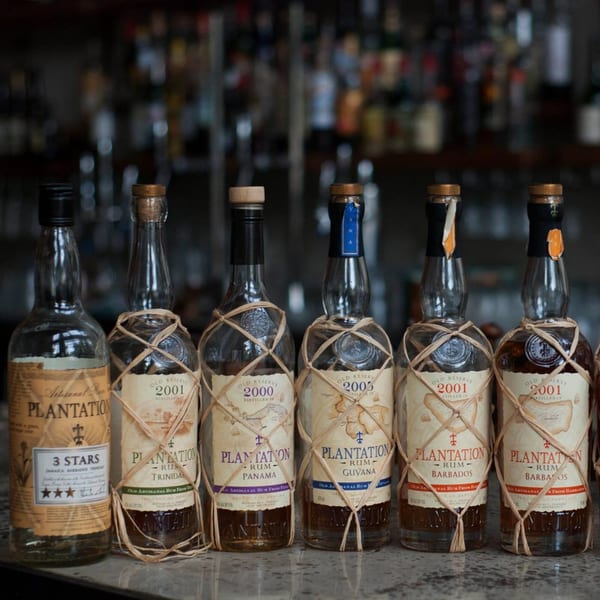 A collection of Plantation rum bottles, some wrapped in raffia, displayed on a bar.