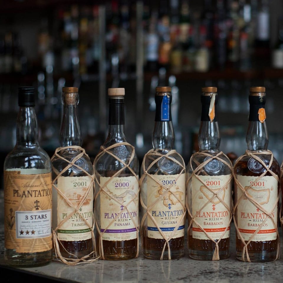 A collection of Plantation rum bottles, some wrapped in raffia, displayed on a bar.