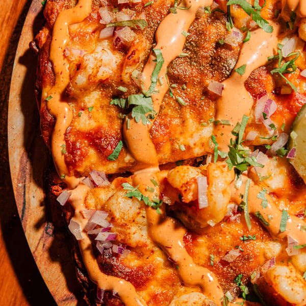 Close-up of Indian shrimp pizza with red sauce, cilantro, and diced red onions.
