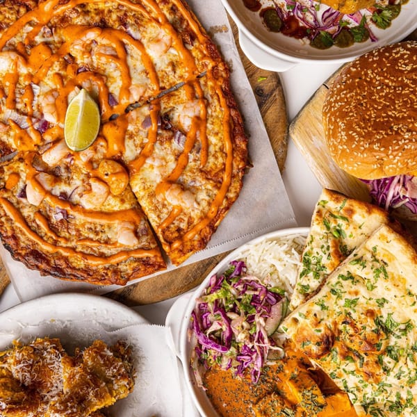 Overhead view of various Indian dishes, including a shrimp pizza, naan, rice, and a burger.