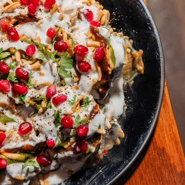 Close-up of Indian chaat with yogurt, chutneys, pomegranate seeds, and crispy toppings.